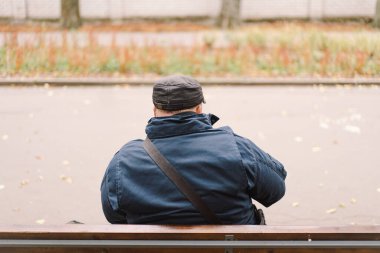 Bir saksafoncu, sonbaharda yapraklarla çevrili bir bankta otururken sakin bir parkta gösteri yapar.