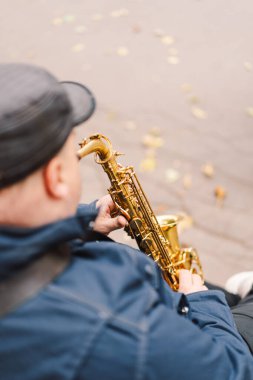 Bir saksafoncu, sonbaharda yapraklarla çevrili bir bankta otururken sakin bir parkta gösteri yapar.