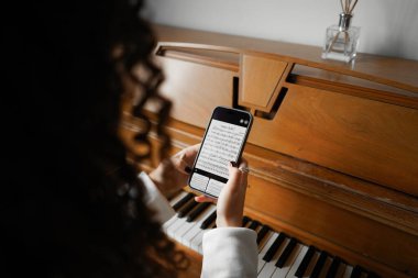 Kıvırcık saçlı bir kadın piyanonun başında oturmuş, güzel ışıklandırılmış oturma odasında yarattığı müziğin keyfini çıkarıyor..