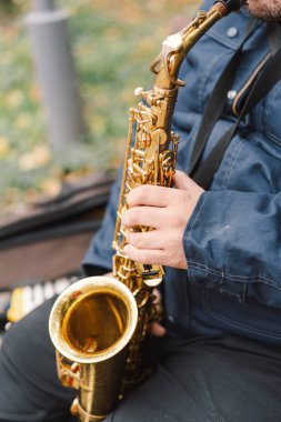 Bir saksafoncu, sonbaharda yapraklarla çevrili bir bankta otururken sakin bir parkta gösteri yapar.