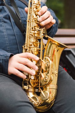 Bir saksafoncu, sonbaharda yapraklarla çevrili bir bankta otururken sakin bir parkta gösteri yapar.