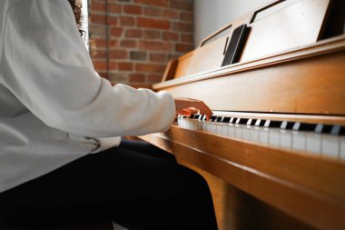 Kıvırcık saçlı bir kadın piyanonun başında oturmuş, güzel ışıklandırılmış oturma odasında yarattığı müziğin keyfini çıkarıyor..