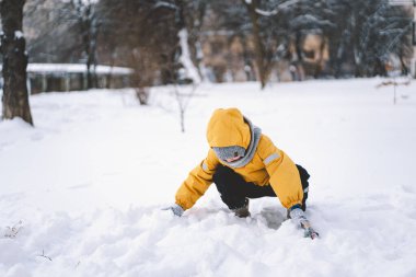 Parlak sarı ceketli neşeli bir çocuk kış boyunca taze karda oynuyor.