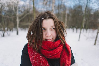 Kırmızı eşarplı gülümseyen bir kadın, parlak mavi gökyüzünün altındaki sakin bir ormanda karlı bir kış gününün tadını çıkarıyor. Noel ve Yeni Yıl Kutlama Konsepti.