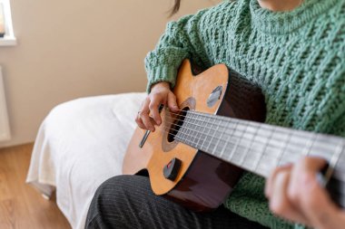 Sıcak bir odada gitar çalan bir kadın. Güneş ışığı yumuşak gölgeler bırakır, müzikal ifadesi için sakin bir atmosfer yaratır..