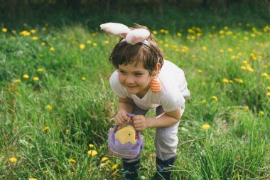 Yumurta sepeti ve tavşan kulaklı komik çocuk güneşli bahar bahçesinde Paskalya yumurtası avında. Paskalya yumurtası avlamak