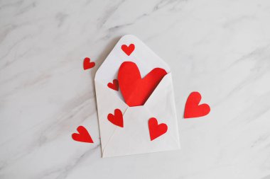 Masanın üzerinde kalp şeklinde konfeti ve kırmızı bir gülle süslenmiş beyaz bir zarf var. Özel bir günde aşkı ifade etmek için mükemmel bir ortam. Sevgililer Günün kutlu olsun.
