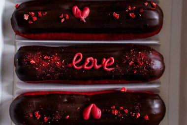 Delicious chocolate eclairs with love decorations ready to be enjoyed alongside a cup of coffee. Romantic gesture. Happy Valentines Day. clipart