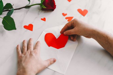 Bir adam yürekten bir not yazar. Seni kırmızı kalplerle çevrili bir zarfın üzerinde sevdiğimi söyler. Bir bilye masasında tek bir gül romantik bir atmosfer yaratır. Romantik bir jest. Sevgililer Günün kutlu olsun..