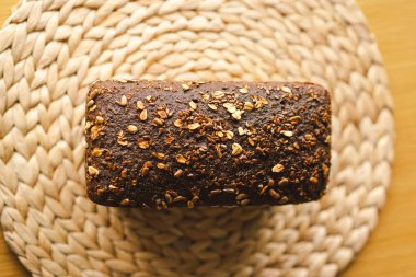 Ekmek, taze pişmiş ve hala sıcak, ahşap bir yüzeye istiflenmiştir. Ekmek susam ve ayçiçeğiyle kaplıdır, kırsal ve lezzetli bir dokunuş katar..