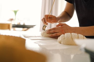 Kadın eli becerikli bir şekilde yuvarlak hamur somunu yüzeyi siler, ekmek pişirmek için mayalı ekmek hazırlar. Parlak mutfak ortamı sıcak bir atmosfer ve taze malzemeler sağlıyor..