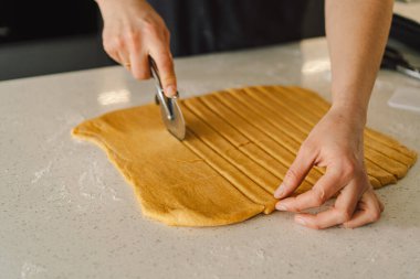 Günlük giysiler içindeki bir kadın hamur işini hazırlar. Memnun ve odaklanmış görünüyor, ışık dolu bir mutfakta pişirme sürecinin tadını çıkarıyor..