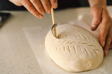 Kadın eli becerikli bir şekilde yuvarlak hamur somunu yüzeyi siler, ekmek pişirmek için mayalı ekmek hazırlar. Parlak mutfak ortamı sıcak bir atmosfer ve taze malzemeler sağlıyor..