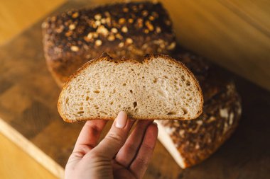 Ekmek, taze pişmiş ve hala sıcak, ahşap bir yüzeye istiflenmiştir. Ekmek susam ve ayçiçeğiyle kaplıdır, kırsal ve lezzetli bir dokunuş katar..