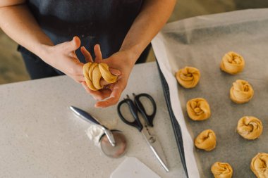 Günlük giysiler içindeki bir kadın hamur işini hazırlar. Memnun ve odaklanmış görünüyor, ışık dolu bir mutfakta pişirme sürecinin tadını çıkarıyor..