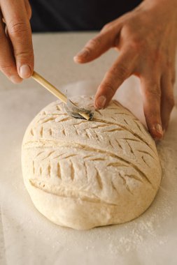 Kadın eli becerikli bir şekilde yuvarlak hamur somunu yüzeyi siler, ekmek pişirmek için mayalı ekmek hazırlar. Parlak mutfak ortamı sıcak bir atmosfer ve taze malzemeler sağlıyor..
