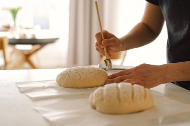 Kadın eli becerikli bir şekilde yuvarlak hamur somunu yüzeyi siler, ekmek pişirmek için mayalı ekmek hazırlar. Parlak mutfak ortamı sıcak bir atmosfer ve taze malzemeler sağlıyor..