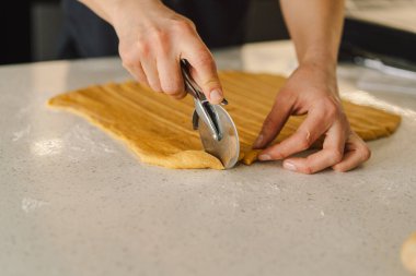 Günlük giysiler içindeki bir kadın hamur işini hazırlar. Memnun ve odaklanmış görünüyor, ışık dolu bir mutfakta pişirme sürecinin tadını çıkarıyor..