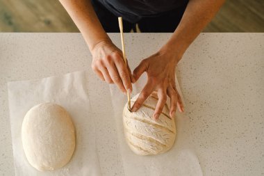 Kadın eli becerikli bir şekilde yuvarlak hamur somunu yüzeyi siler, ekmek pişirmek için mayalı ekmek hazırlar. Parlak mutfak ortamı sıcak bir atmosfer ve taze malzemeler sağlıyor..