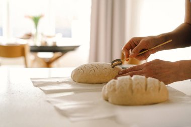 Kadın eli becerikli bir şekilde yuvarlak hamur somunu yüzeyi siler, ekmek pişirmek için mayalı ekmek hazırlar. Parlak mutfak ortamı sıcak bir atmosfer ve taze malzemeler sağlıyor..