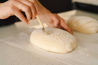 Kadın eli becerikli bir şekilde yuvarlak hamur somunu yüzeyi siler, ekmek pişirmek için mayalı ekmek hazırlar. Parlak mutfak ortamı sıcak bir atmosfer ve taze malzemeler sağlıyor..
