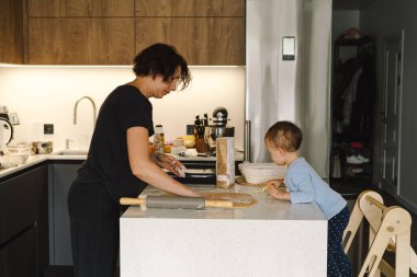 Mutlu aile birlikte fırın hazırlıyor. Anne ve kız çocuk kurabiye pişiriyor ve mutfakta eğleniyorlar. Ev yapımı yemek ve küçük bir yardımcı.