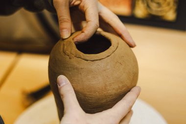 Çömlek atölyesinde kilden bir tencereyi ustalıkla şekillendiren eller. Atölye yaratıcılığı teşvik ediyor ve yeni başlayanlara rahat bir ortamda çömlek teknikleri öğretmeye odaklanıyor..