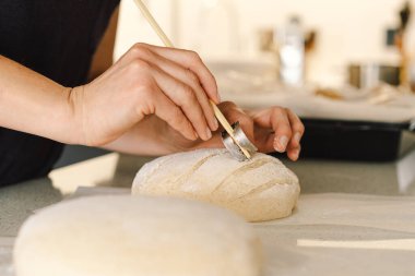Kadın eli becerikli bir şekilde yuvarlak hamur somunu yüzeyi siler, ekmek pişirmek için mayalı ekmek hazırlar. Parlak mutfak ortamı sıcak bir atmosfer ve taze malzemeler sağlıyor..