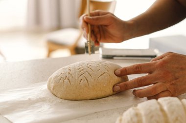 Kadın eli becerikli bir şekilde yuvarlak hamur somunu yüzeyi siler, ekmek pişirmek için mayalı ekmek hazırlar. Parlak mutfak ortamı sıcak bir atmosfer ve taze malzemeler sağlıyor..