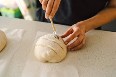 Kadın eli becerikli bir şekilde yuvarlak hamur somunu yüzeyi siler, ekmek pişirmek için mayalı ekmek hazırlar. Parlak mutfak ortamı sıcak bir atmosfer ve taze malzemeler sağlıyor..
