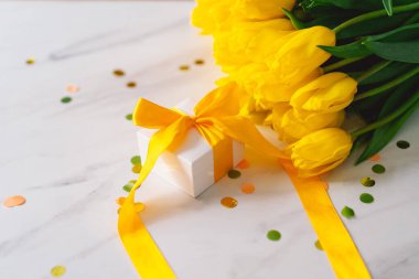 Uzun sarı kurdeleli hediye kutusu ve açık arkaplanda laleler.