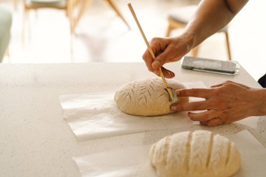 Kadın eli becerikli bir şekilde yuvarlak hamur somunu yüzeyi siler, ekmek pişirmek için mayalı ekmek hazırlar. Parlak mutfak ortamı sıcak bir atmosfer ve taze malzemeler sağlıyor..