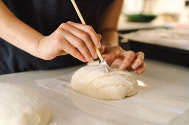Kadın eli becerikli bir şekilde yuvarlak hamur somunu yüzeyi siler, ekmek pişirmek için mayalı ekmek hazırlar. Parlak mutfak ortamı sıcak bir atmosfer ve taze malzemeler sağlıyor..