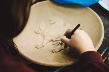Bir insan, bir sanat stüdyosundaki dairesel kil parçasına ayrıntılı desenler kazımaya odaklanır. Aletler ve malzemeler, sanatsal ortamı geliştirmek için düzenlenmiştir..