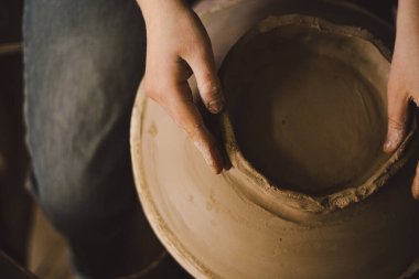Çömlek atölyesinde kilden bir tencereyi ustalıkla şekillendiren eller. Atölye yaratıcılığı teşvik ediyor ve yeni başlayanlara rahat bir ortamda çömlek teknikleri öğretmeye odaklanıyor..