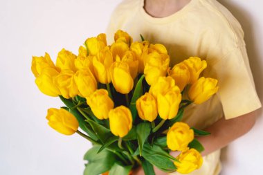 Bir çocuk elinde büyük bir buket sarı lale ile evde duruyor, yüzünde kocaman bir gülümsemeyle mutluluk saçıyor. Parlak atmosfer neşe ve sıcaklığı yansıtır. Anneler Günü ve Bahar Konsepti