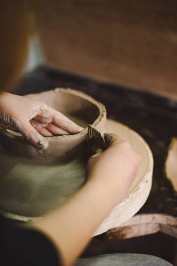 Çömlek atölyesinde kilden bir tencereyi ustalıkla şekillendiren eller. Atölye yaratıcılığı teşvik ediyor ve yeni başlayanlara rahat bir ortamda çömlek teknikleri öğretmeye odaklanıyor..
