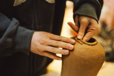 Çömlek atölyesinde kilden bir tencereyi ustalıkla şekillendiren eller. Atölye yaratıcılığı teşvik ediyor ve yeni başlayanlara rahat bir ortamda çömlek teknikleri öğretmeye odaklanıyor..