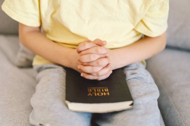 Bir çocuk kutsal kitabı okuyor ve dua ediyor ya da meditasyon yapıyor. Hıristiyanlık, din ve inanç kavramı.