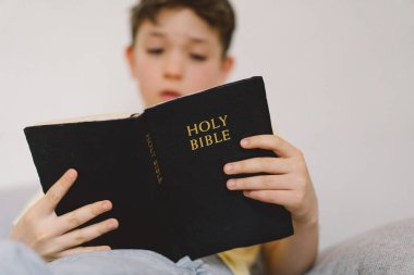 Bir çocuk kutsal kitabı okuyor ve dua ediyor ya da meditasyon yapıyor. Hıristiyanlık, din ve inanç kavramı.