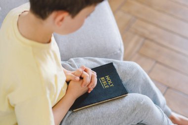 Bir çocuk kutsal kitabı okuyor ve dua ediyor ya da meditasyon yapıyor. Hıristiyanlık, din ve inanç kavramı.