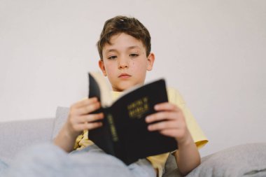 Bir çocuk kutsal kitabı okuyor ve dua ediyor ya da meditasyon yapıyor. Hıristiyanlık, din ve inanç kavramı.