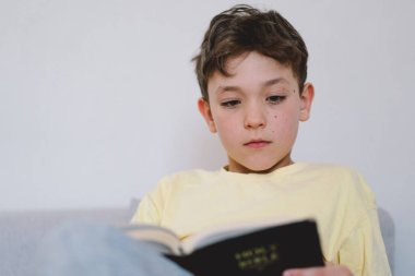 Bir çocuk kutsal kitabı okuyor ve dua ediyor ya da meditasyon yapıyor. Hıristiyanlık, din ve inanç kavramı.