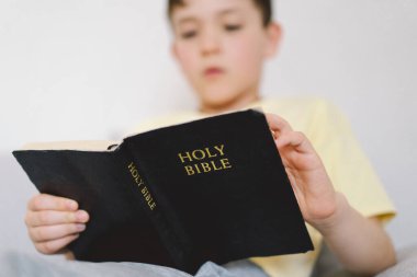 Bir çocuk kutsal kitabı okuyor ve dua ediyor ya da meditasyon yapıyor. Hıristiyanlık, din ve inanç kavramı.
