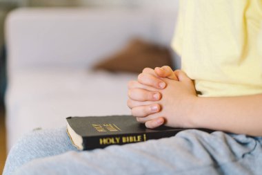 Bir çocuk kutsal kitabı okuyor ve dua ediyor ya da meditasyon yapıyor. Hıristiyanlık, din ve inanç kavramı.