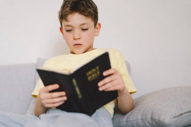 Bir çocuk kutsal kitabı okuyor ve dua ediyor ya da meditasyon yapıyor. Hıristiyanlık, din ve inanç kavramı.