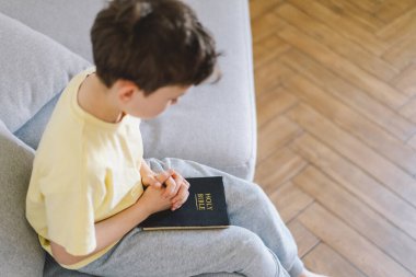 Bir çocuk kutsal kitabı okuyor ve dua ediyor ya da meditasyon yapıyor. Hıristiyanlık, din ve inanç kavramı.