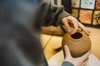 Çömlek atölyesinde kilden bir tencereyi ustalıkla şekillendiren eller. Atölye yaratıcılığı teşvik ediyor ve yeni başlayanlara rahat bir ortamda çömlek teknikleri öğretmeye odaklanıyor..