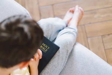 Bir çocuk kutsal kitabı okuyor ve dua ediyor ya da meditasyon yapıyor. Hıristiyanlık, din ve inanç kavramı.