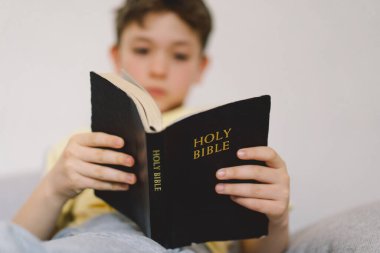 Bir çocuk kutsal kitabı okuyor ve dua ediyor ya da meditasyon yapıyor. Hıristiyanlık, din ve inanç kavramı.